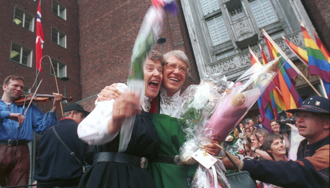 Fem par inngikk partnerskap samtidig i Oslo Rådhus 6. august 1993. På bildet ser vi Kim Friele (tv) og Wenche Lowzow omringet av jublende mennesker med regnbueflagg etter seremonien inne i Rådhuset. I bakgrunnen spiller Øyvind Rauset fele. Foto: Kim Friele/Skeivt arkiv. Fem par inngikk partnerskap samtidig i Oslo Rådhus 6. august 1993. På bildet ser vi Kim Friele (tv) og Wenche Lowzow omringet av jublende mennesker med regnbueflagg etter seremonien inne i Rådhuset. I bakgrunnen spiller Øyvind Rauset fele. Foto: Kim Friele/Skeivt arkiv.