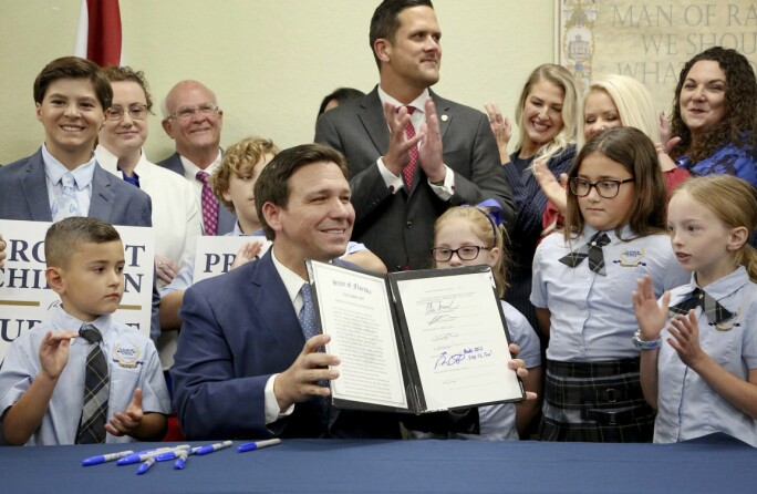 En smilende Ron DeSantis, guvernør i Florida, viser den signerte loven under en pressekonferanse på en barneskole i Shady Hills.