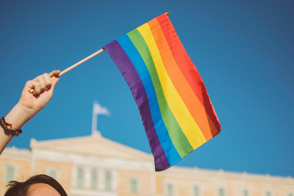 En paradedeltaker flagger med regnbuefargene foran parlamentet i Hellas under pride i Athen i 2019.