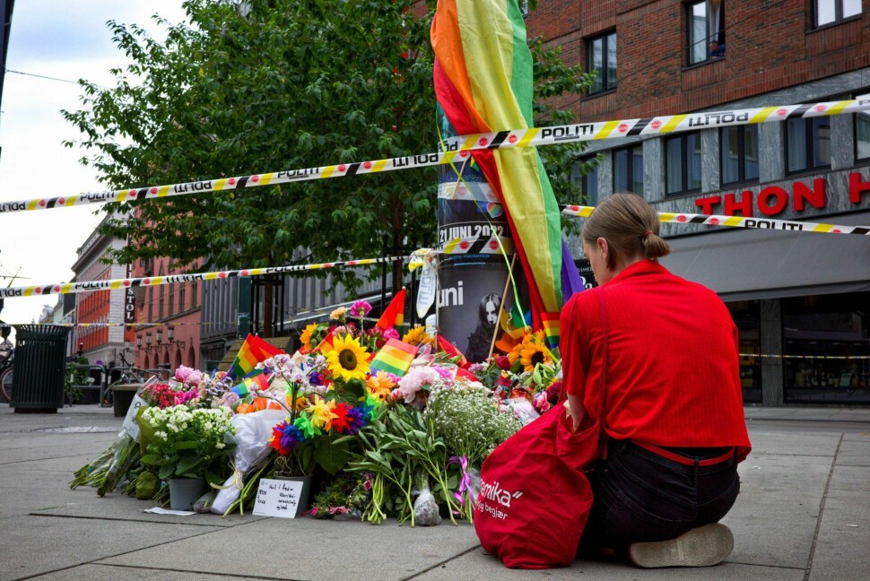 En person sitter på bakken foran blomster, hilsener og prideflagg lagt ned på C. J. Hambros plass etter skyteepisoden i Oslo.